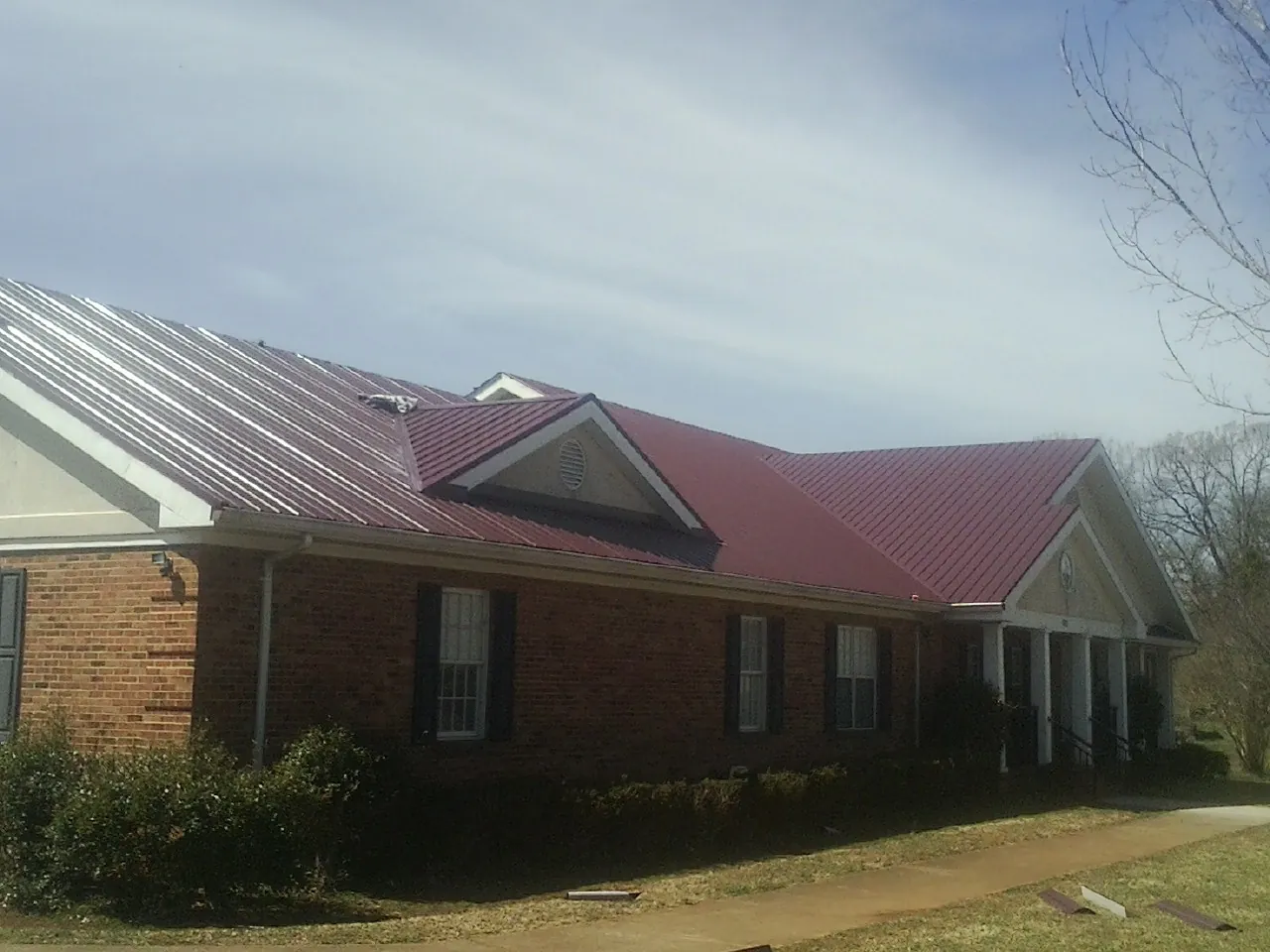 Red metal roof with gabled entries on a long brick building, from a Hail Damage Roof Repair job in Three Springs