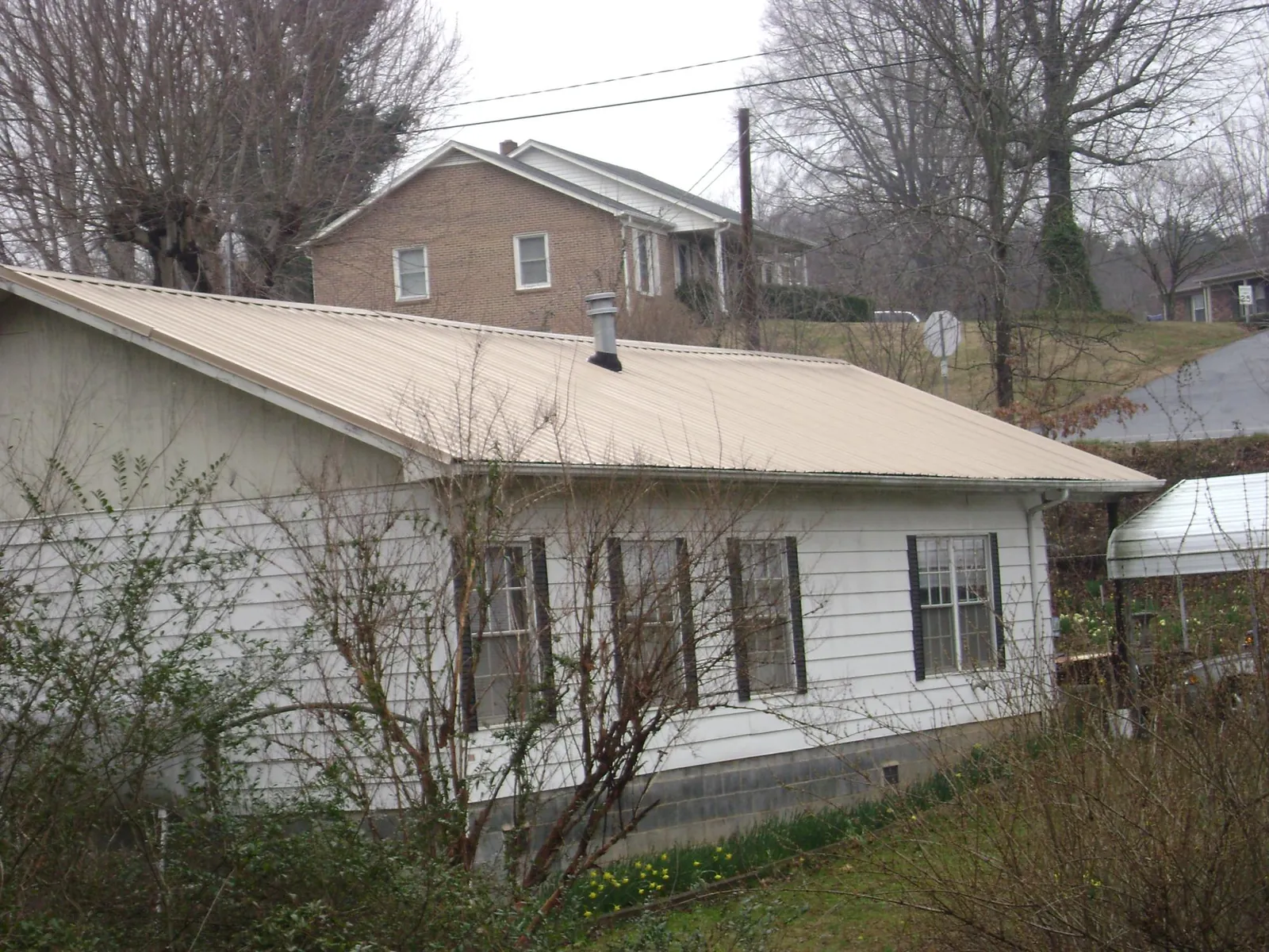 Tan metal roof on a white sided house set into a hillside — Commercial Roofing by Roofing Brothers in Three Springs